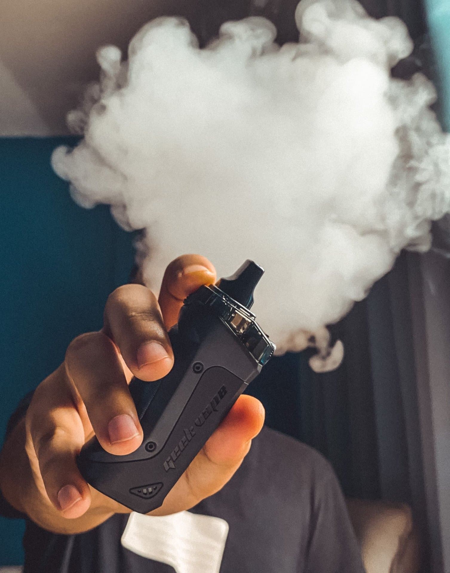 Close-up of a hand holding a vape device with a large cloud of vapour