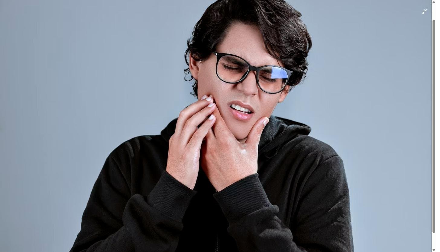 Young man wincing and holding his jaw with his hand, showing signs of tooth or gum pain