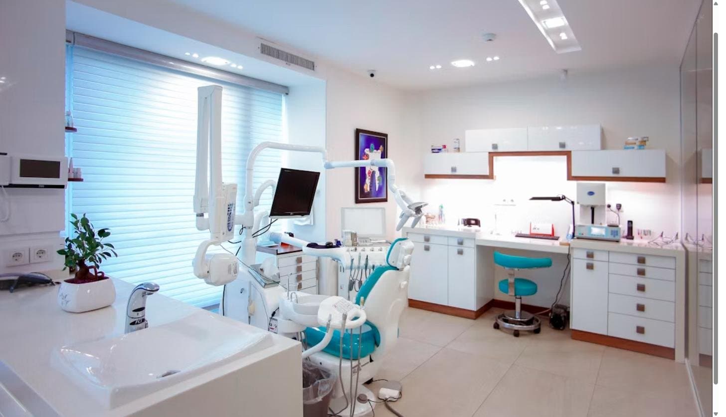 Modern dental treatment room with panoramic X-ray equipment, dental chair, and cabinetry in a well-lit clinic