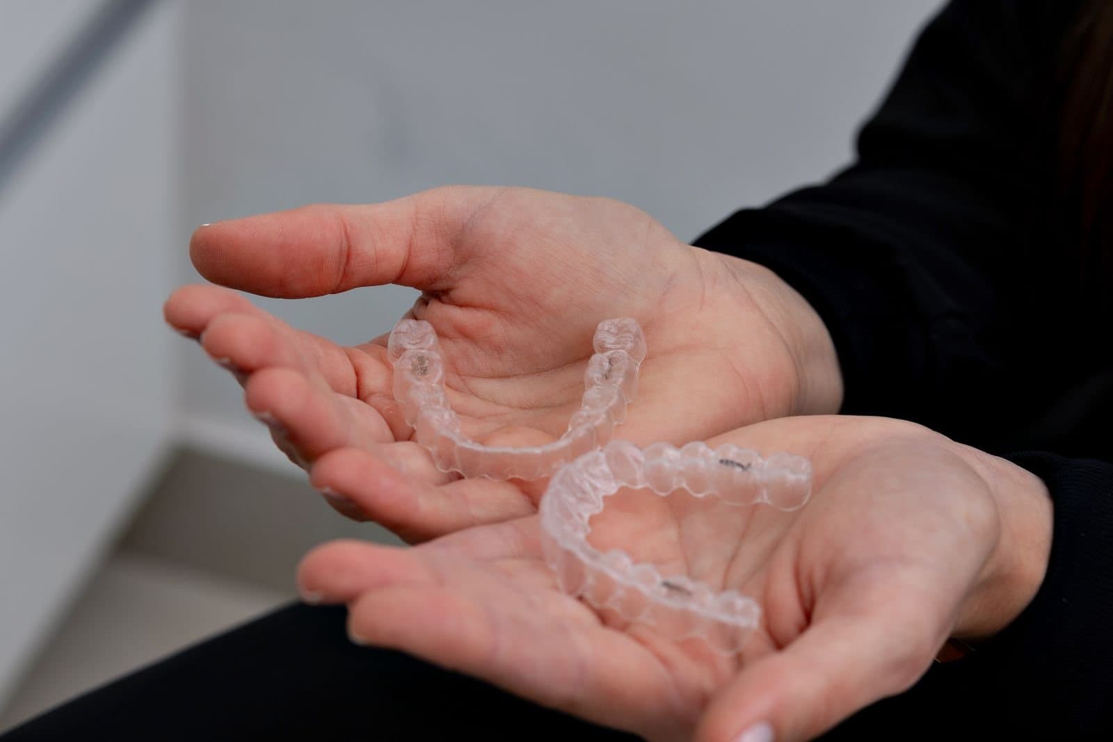A hand holding two clear plastic aligner trays, the removable alternative to fixed braces