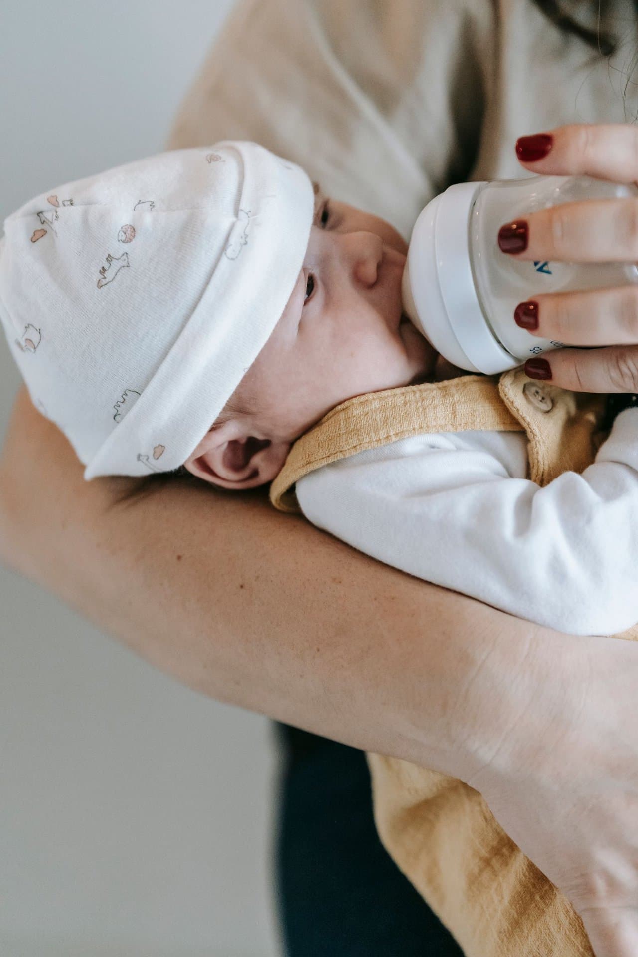 Parent bottle-feeding a newborn baby wearing a knit hat