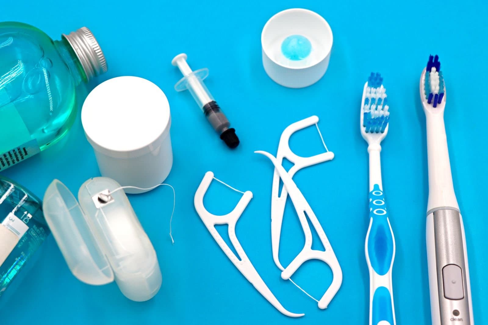 Assorted oral hygiene products including mouthwash, floss, and toothbrushes on a blue background